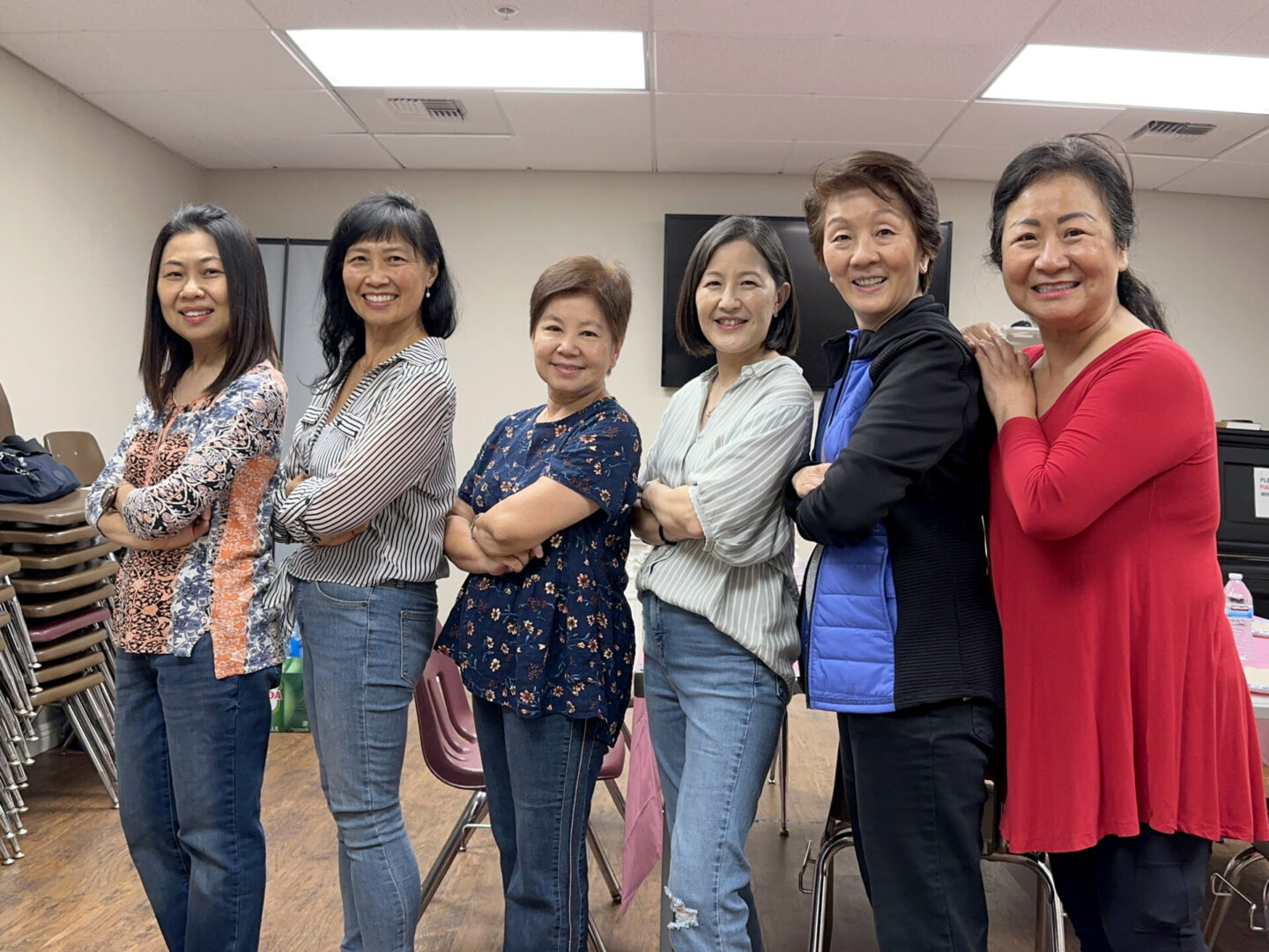 Six women standing side by side with arms crossed, smiling indoors.