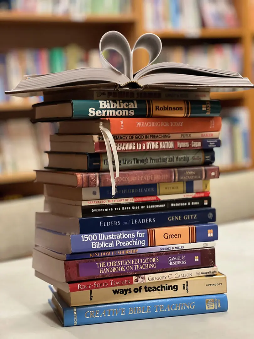 Stack of books on preaching and teaching with open book pages shaped as a heart.